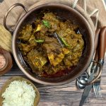 Green Mutton Curry in a kadhai with rice and whole spices on the side.